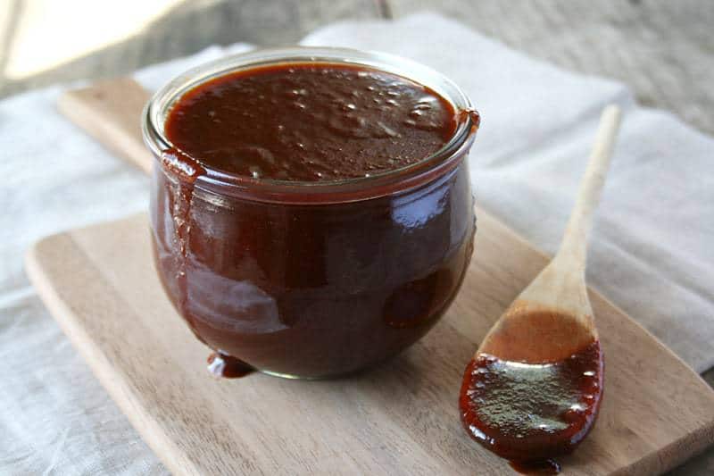 A pot of BBQ sauce on a wooden surface with a spoon