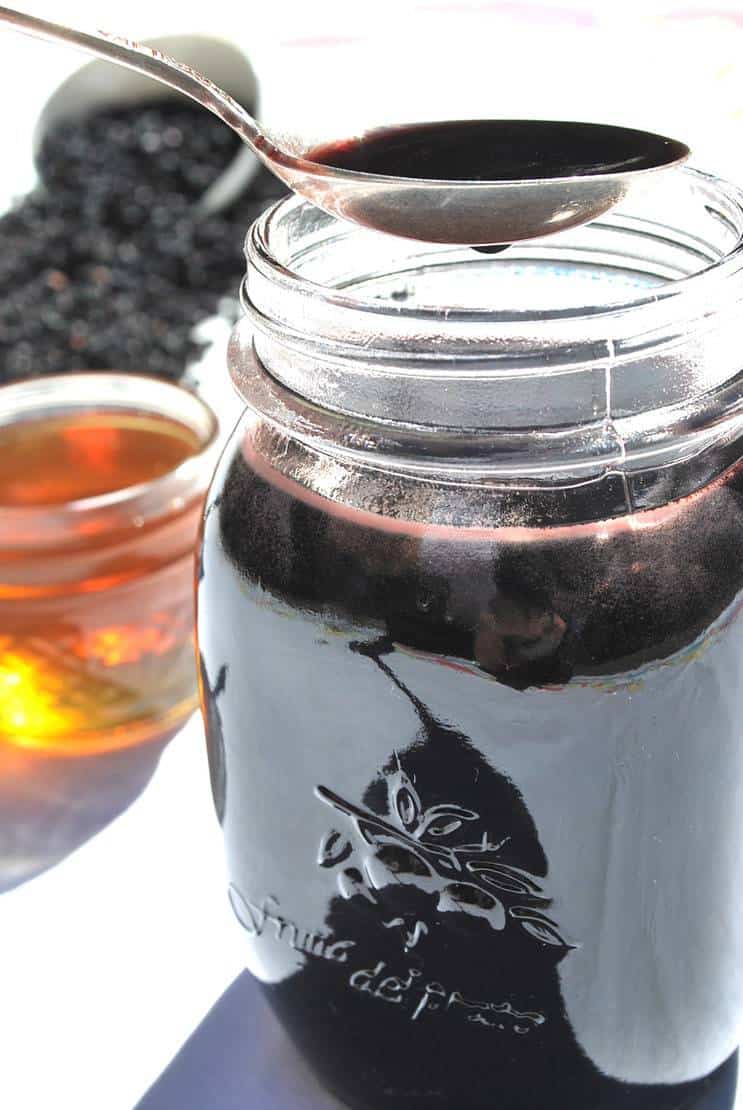 close up of homemade elderberry syrup in jar and on spoon