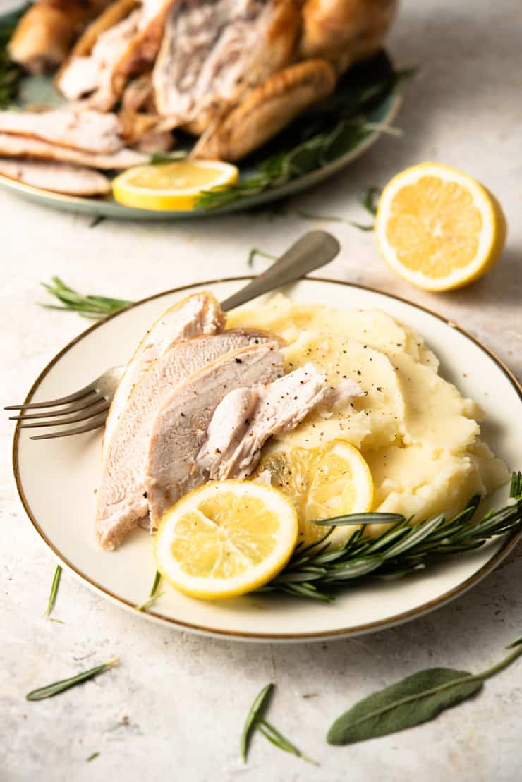 Herb roasted chicken cut into slices on a plate with mashed potatoes and lemon