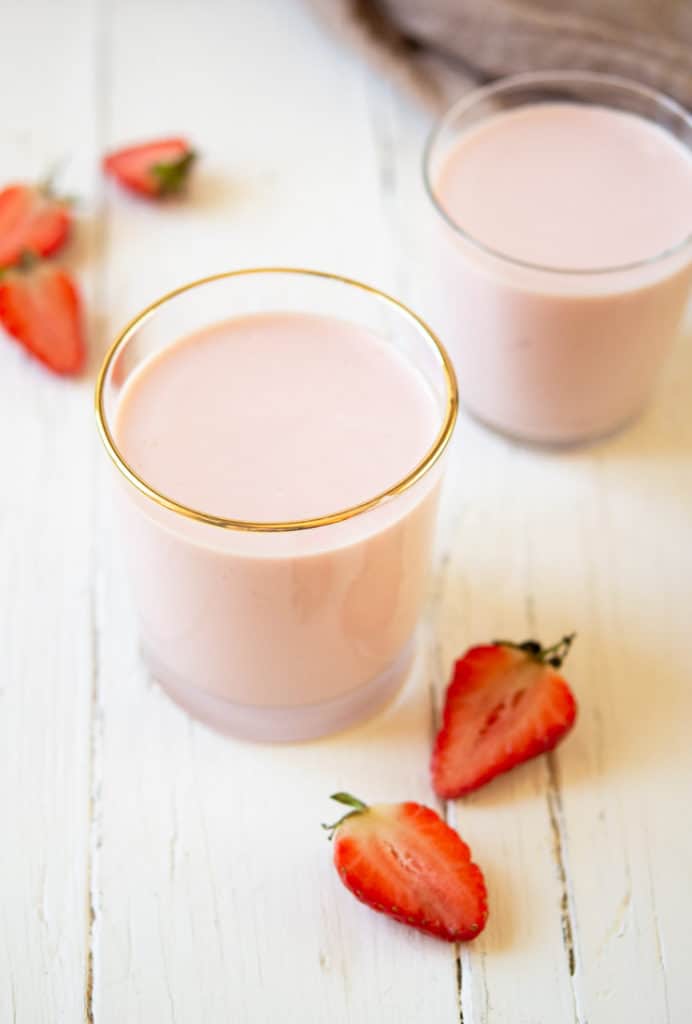 Two glasses of drinkable yogurt on a white wooden surface