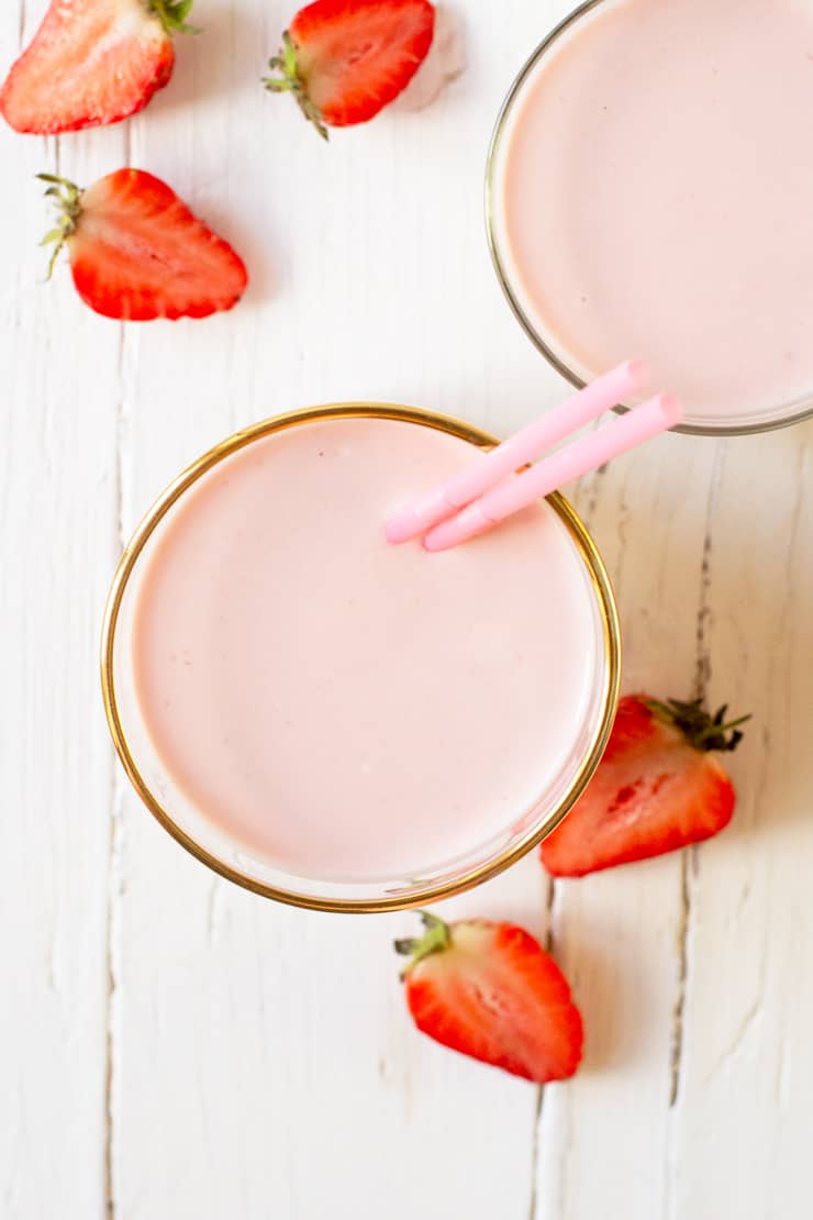 An overhead shot of strawberry drinkable yogurt in a glass with strawberries at the side