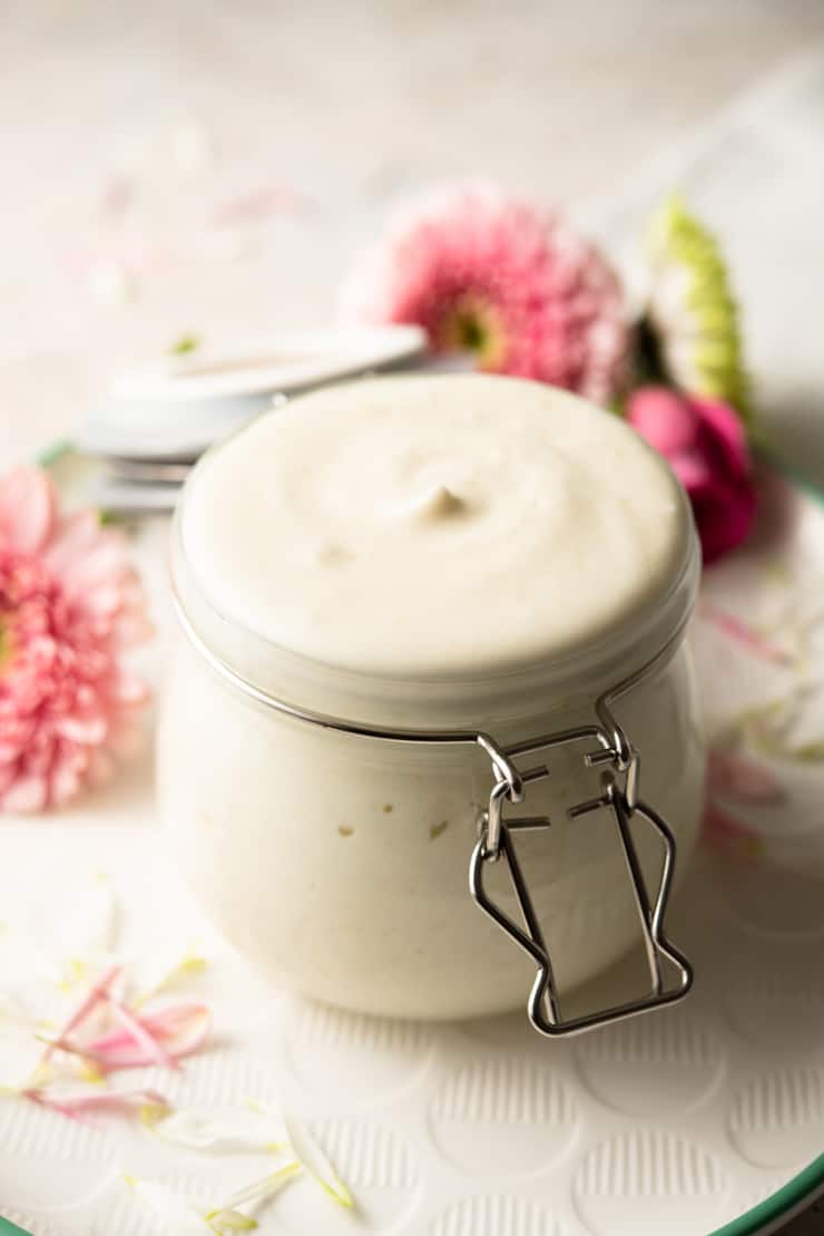 A close up of a jar of homemade lotion with flowers in the background