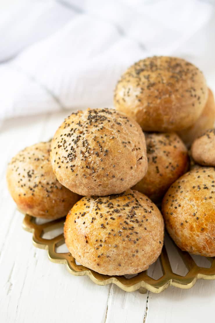 Homemade hamburger buns stacked on top of each other sitting on a white wooden surface