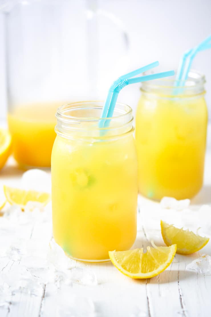 Two mason jars with natural pineapple lemonade and blue straws on a white surface