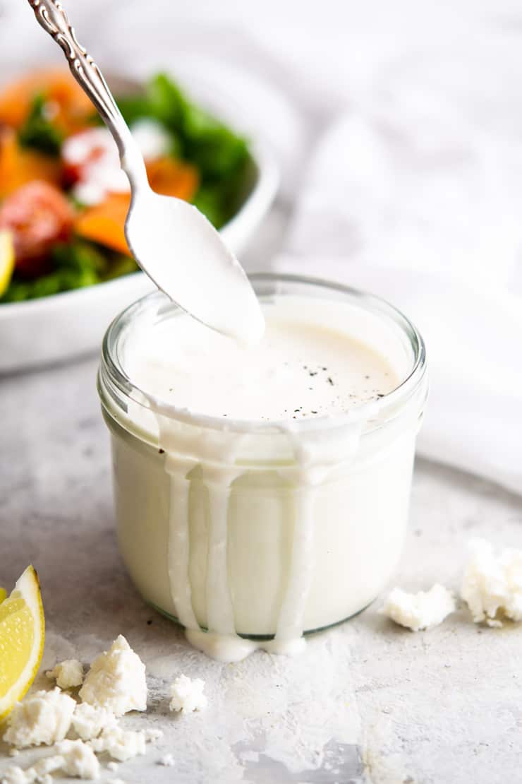 A jar of creamy feta yogurt dressing with a salad in the background