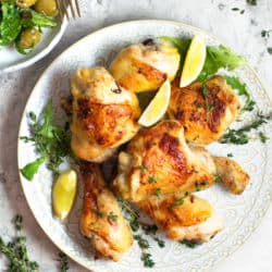 Greek chicken on a plate with lemon wedges and thyme