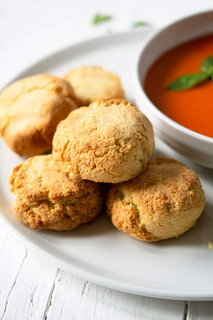 Almond flour cheddar biscuits on a white plate with a bowl of tomato soup in the background