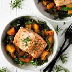 An overhead shot of easy salmon butternut squash and kale in a white bowl topped with rosemary