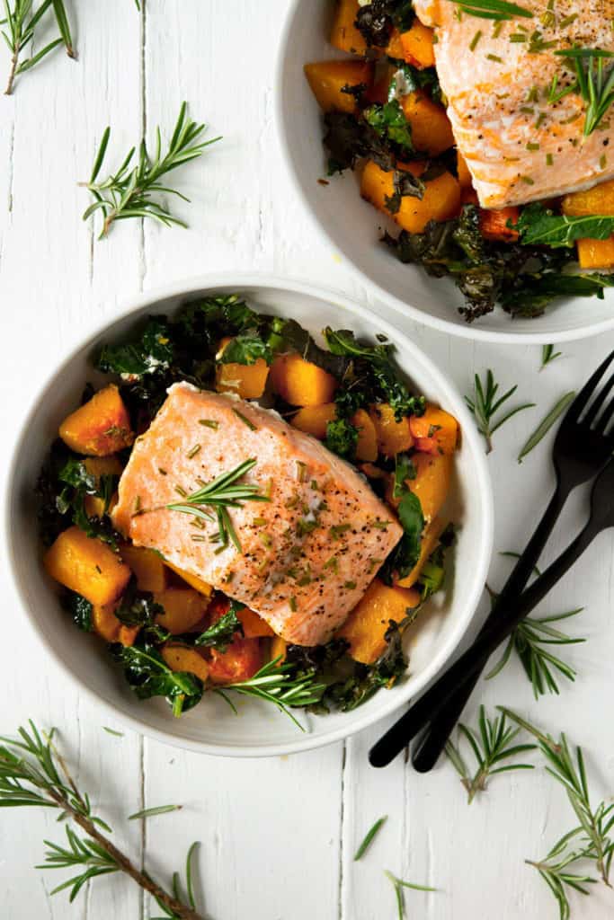 An overhead shot of easy salmon butternut squash and kale in a white bowl topped with rosemary