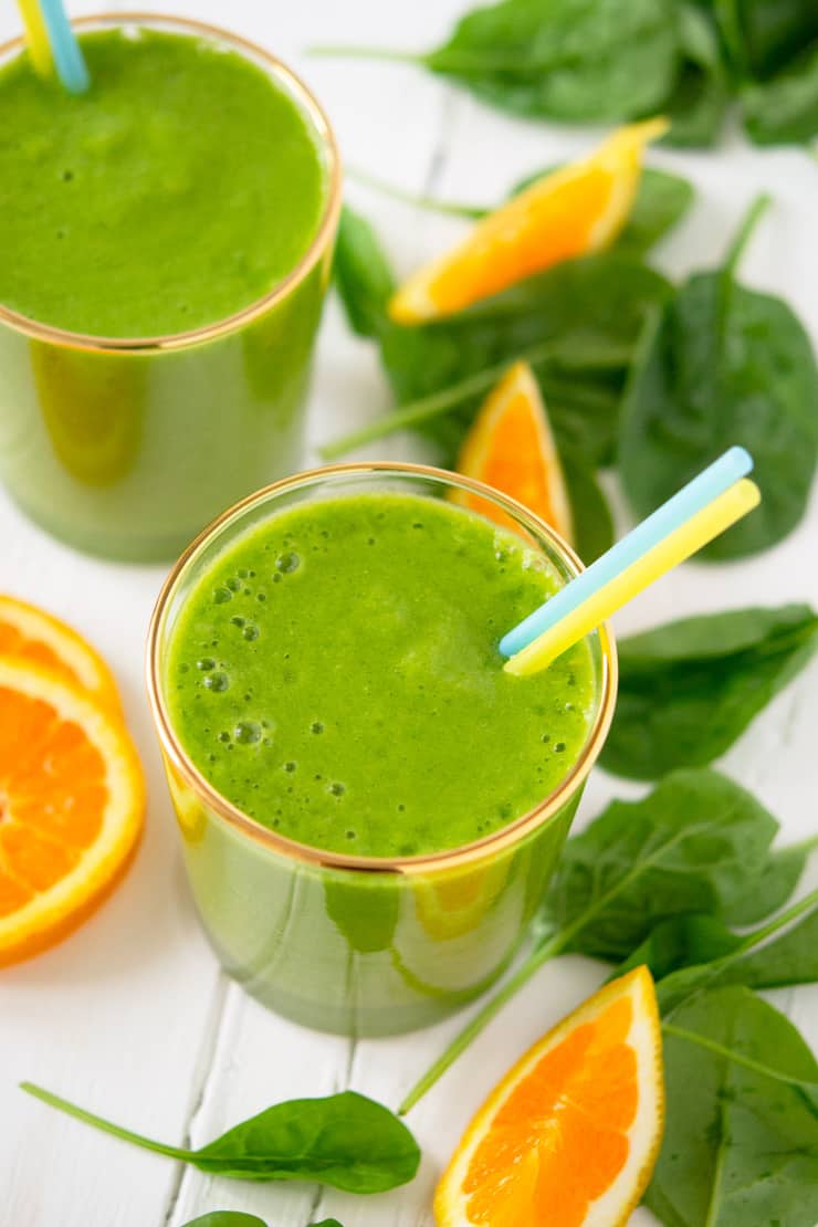 A close up of an orange pineapple green smoothie in a glass with two straws