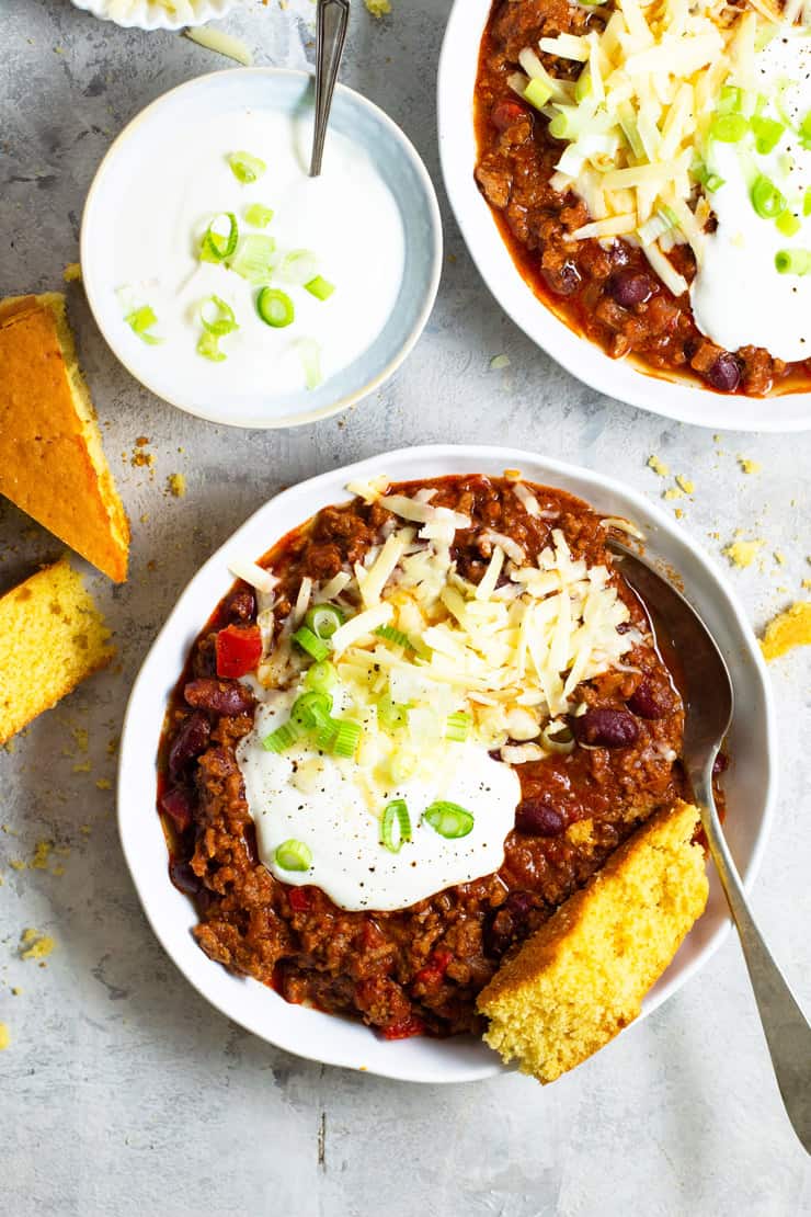 An overhead shot of two bowls of real Texas chili topped with sour cream, cheese and green onions