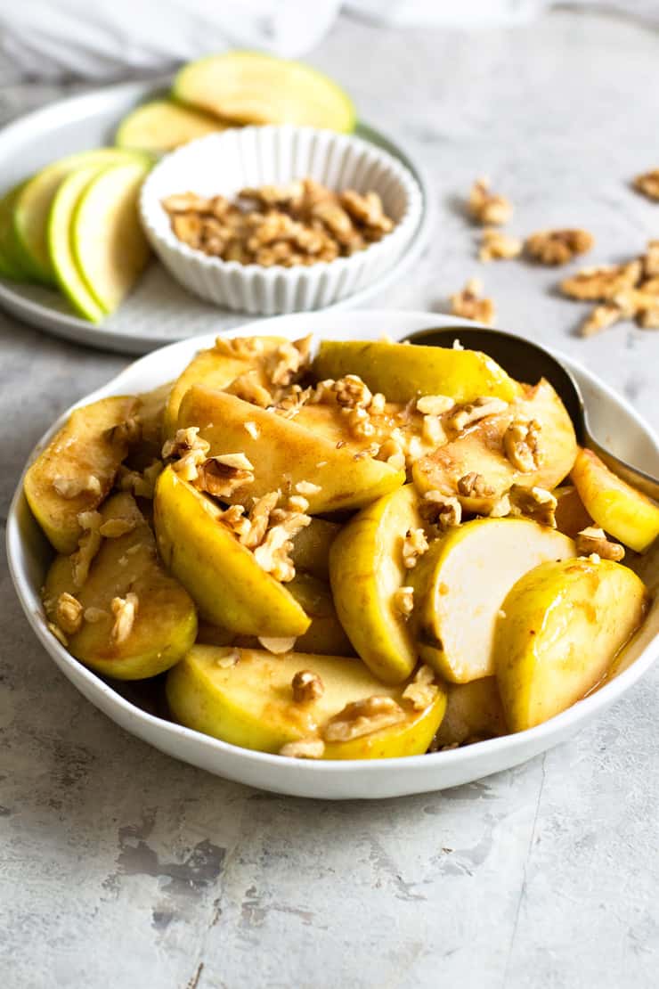 A close up of a bowl of baked apples topped with walnuts