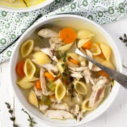 An overhead shot of chicken noodle soup in a white bowl with a spoon