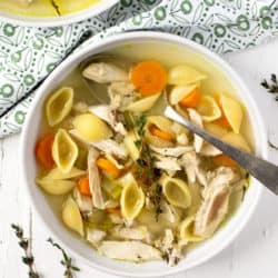 An overhead shot of chicken noodle soup in a white bowl with a spoon