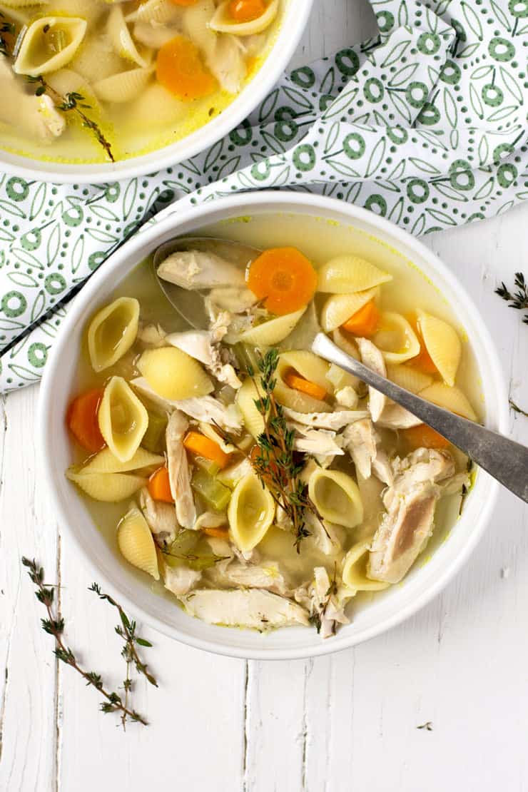 An overhead shot of chicken noodle soup in a white bowl with a spoon