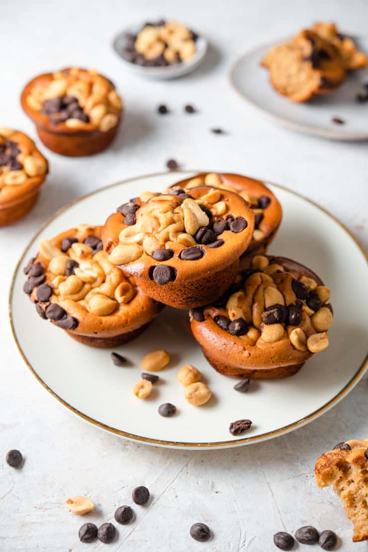 Healthy chocolate chip muffins stacked on a plate with peanuts and choc chips scattered around