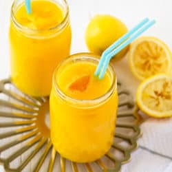 front angle view of two glasses of all natural mango lemonade with teal straws, on gold tray with white background