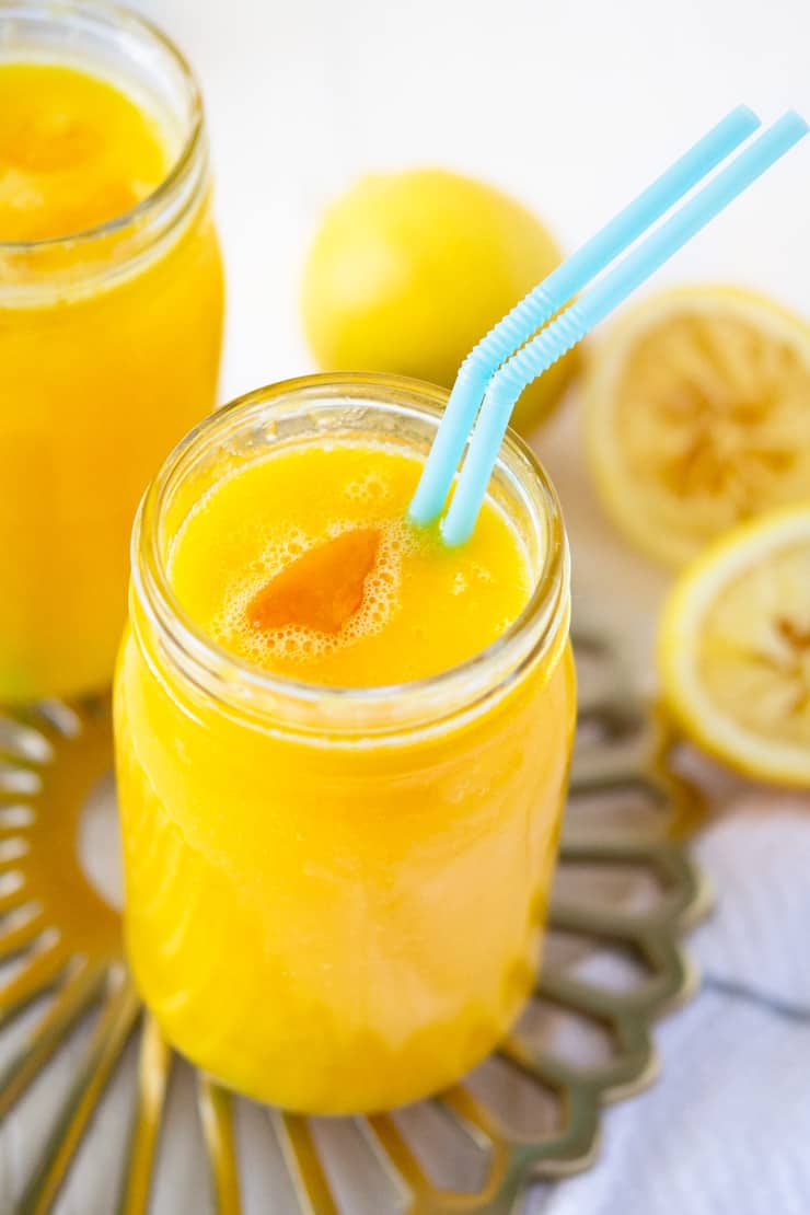 close up of glass of all natural mango lemonade with teal straw, on gold tray