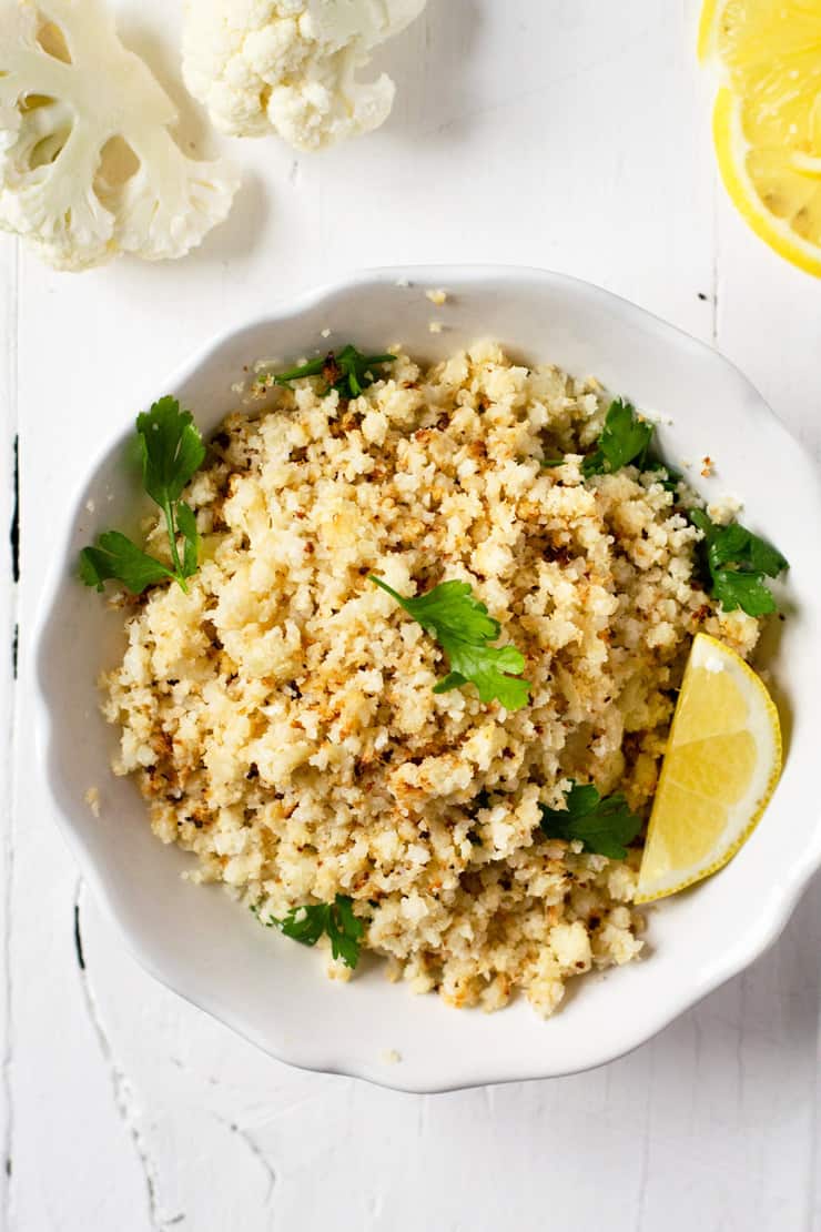 A white bowl of roasted cauliflower rice topped with herbs
