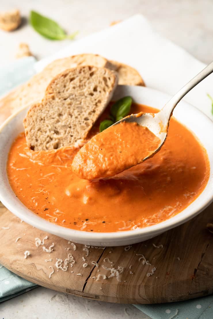 A close up of a spoonful of roasted red pepper soup and slices of bread at the side