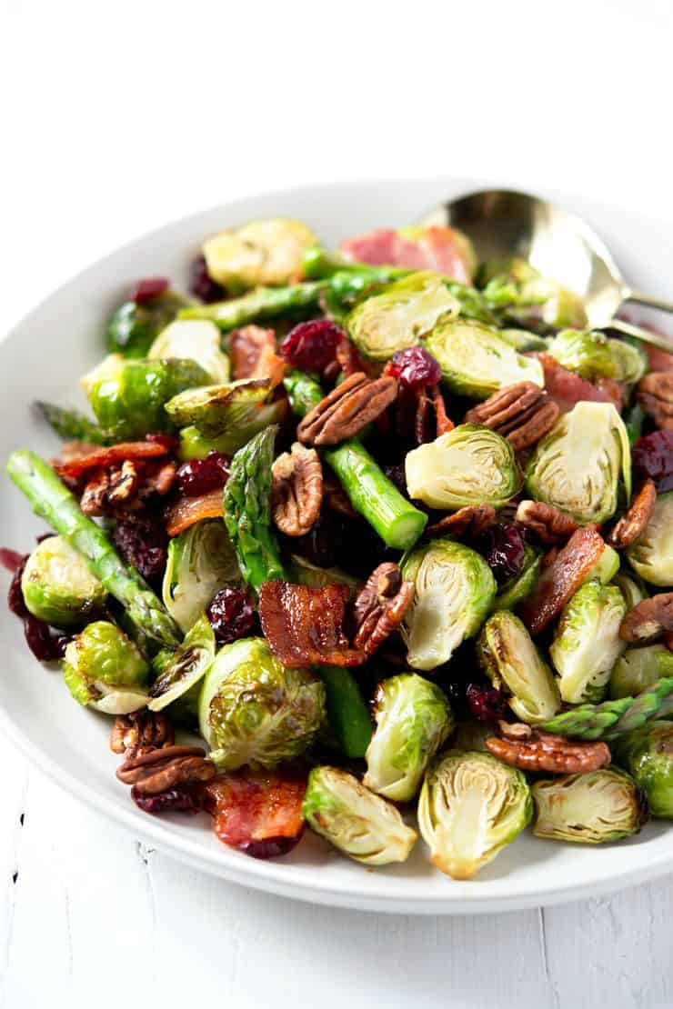 A close up of roasted brussels sprouts with asparagus, bacon and pecans