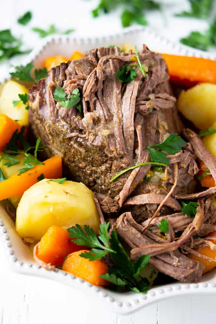 A close up of the best slow cooker beef roast in a serving dish with potatoes and carrots