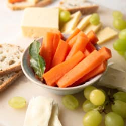 Fermented carrots in bowl with grapes, cheese, and bread scattered around