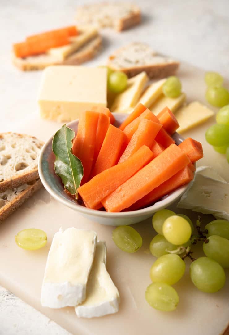 A close up of fermented carrots in a serving dish with cheese and grapes