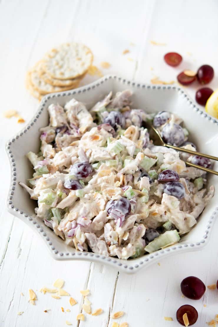 A rotisserie chicken salad in a white dish with grapes and crackers at the side