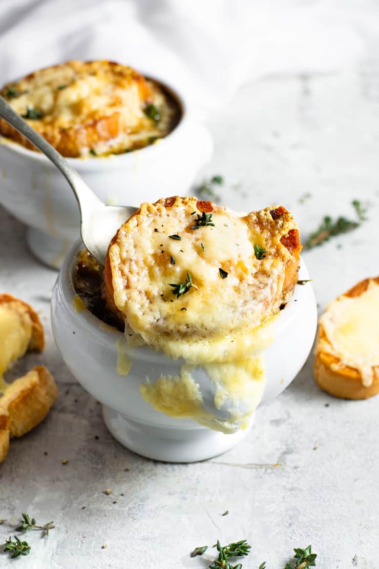 Close up image of the best French Onion Soup in white bowl with melty cheese toast on top 