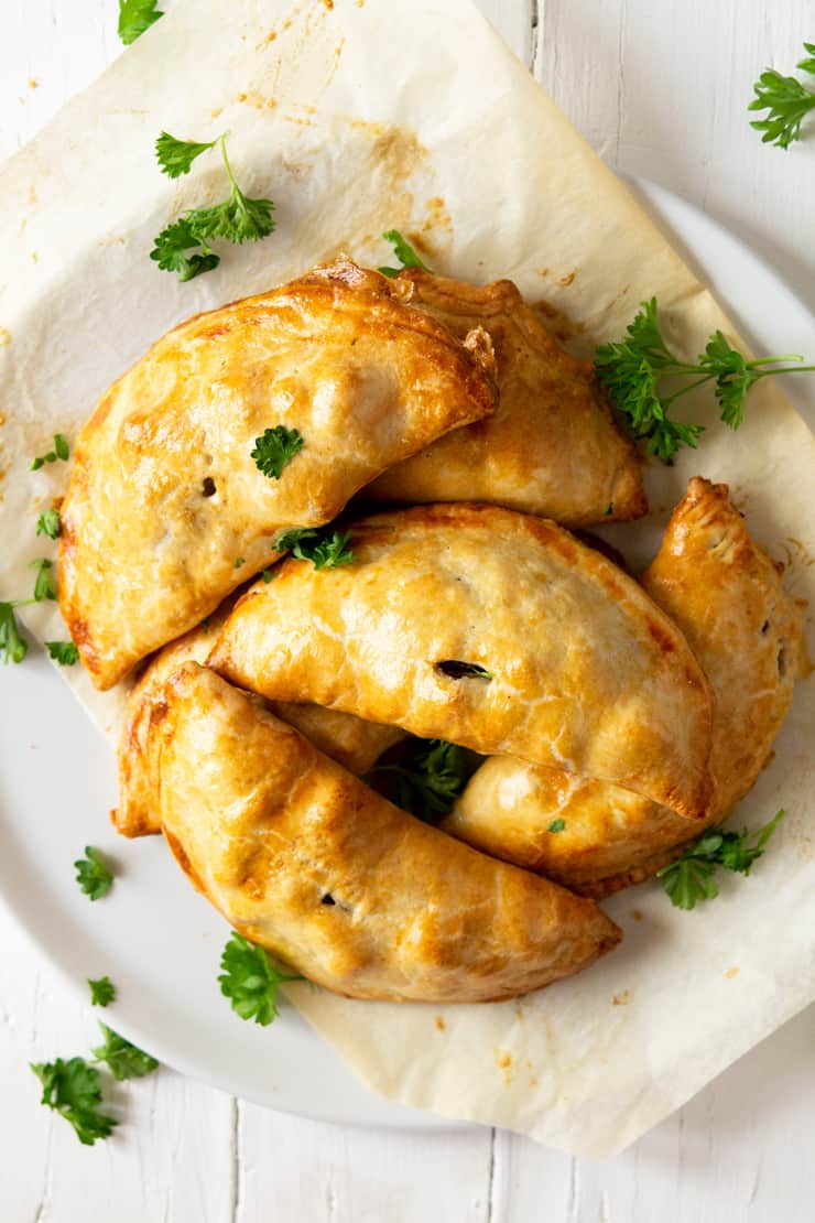 An overhead shot of beef and potato hand pies on a white plate garnished with parsley