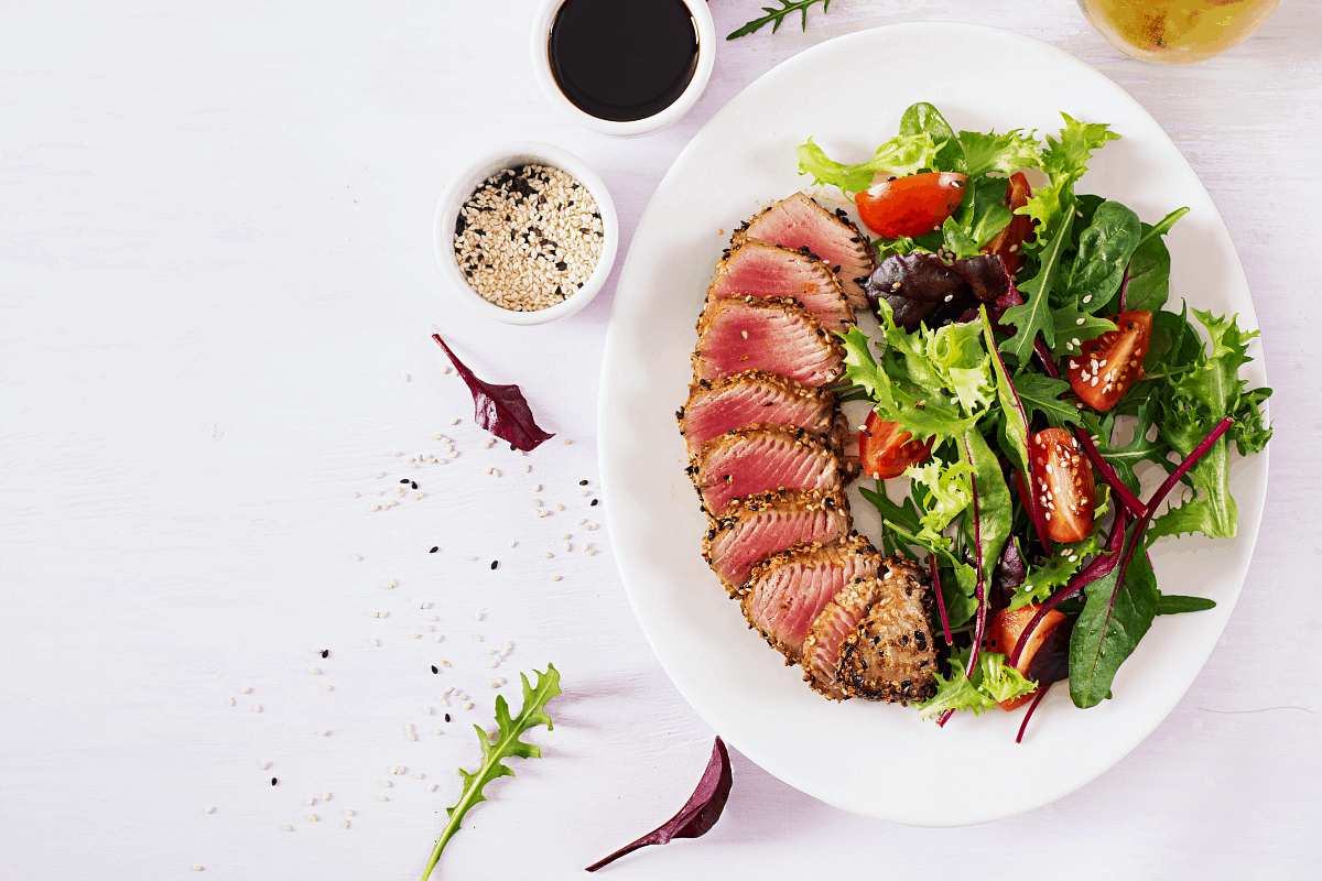 overhead image of large green salad with medium rare Ahi tuna medallions and dressing on side