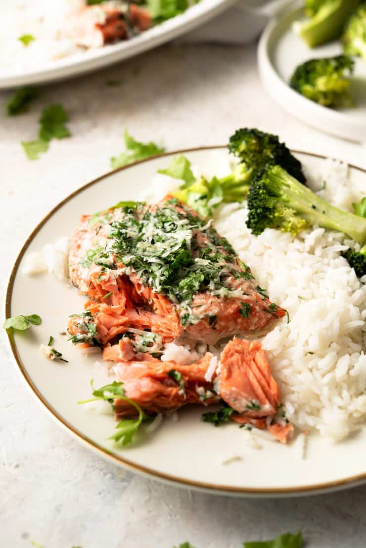 A close up of baked salmon with parmesan crust and herbs on a white plate