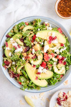 Overhead view of kale and quinoa salad in bowl with avocadoes, cranberries and almonds on white background