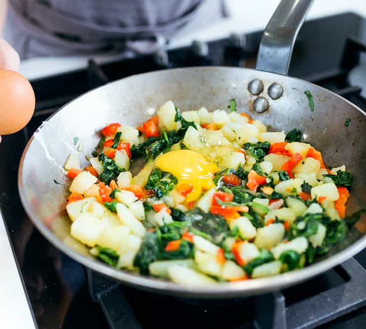 Close-up of hands of a young woman adding egg to vegetables into the pan.