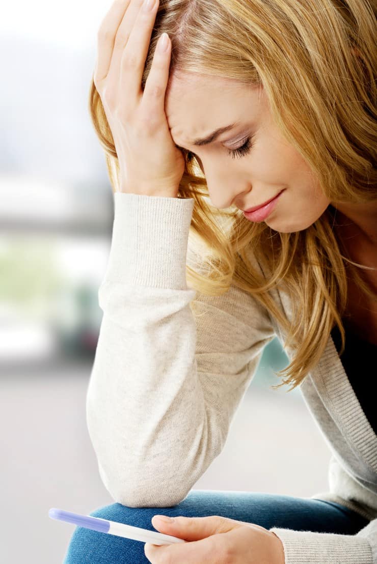 Sad young woman holding pregnancy test.