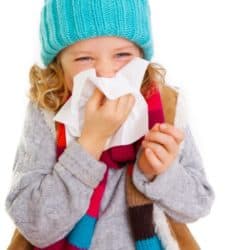 young girl bundled in winter clothing blowing nose