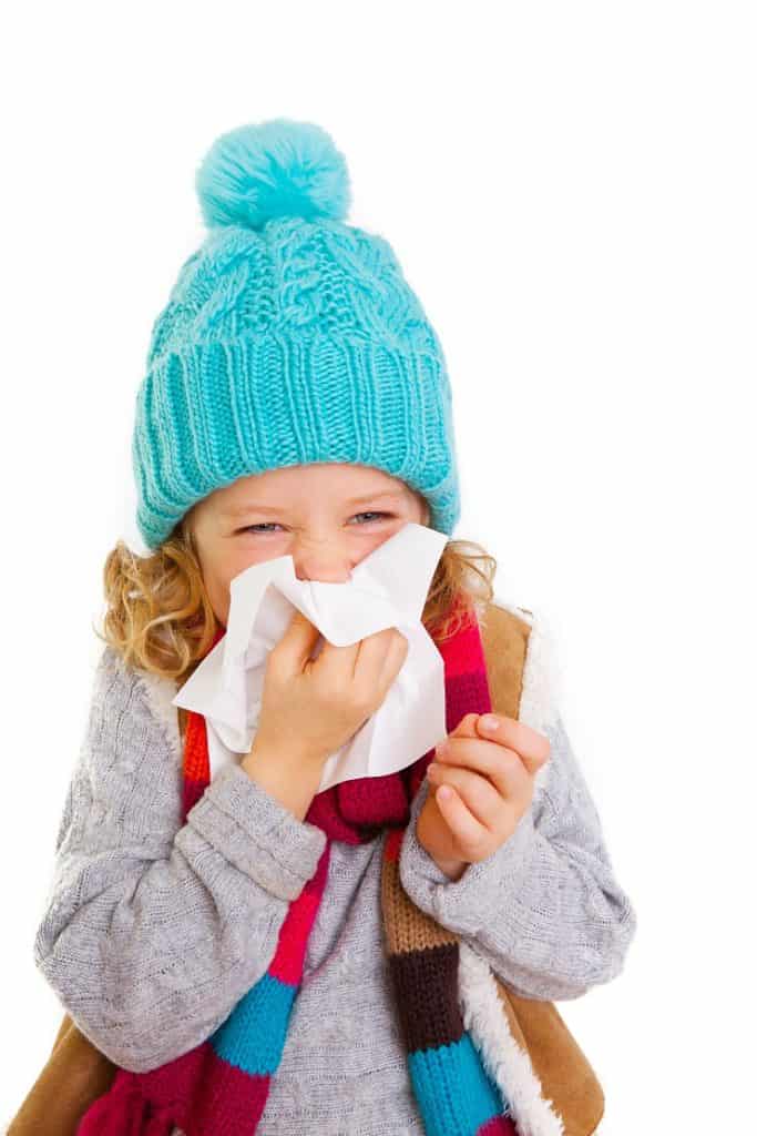 young girl in warm clothing blowing nose