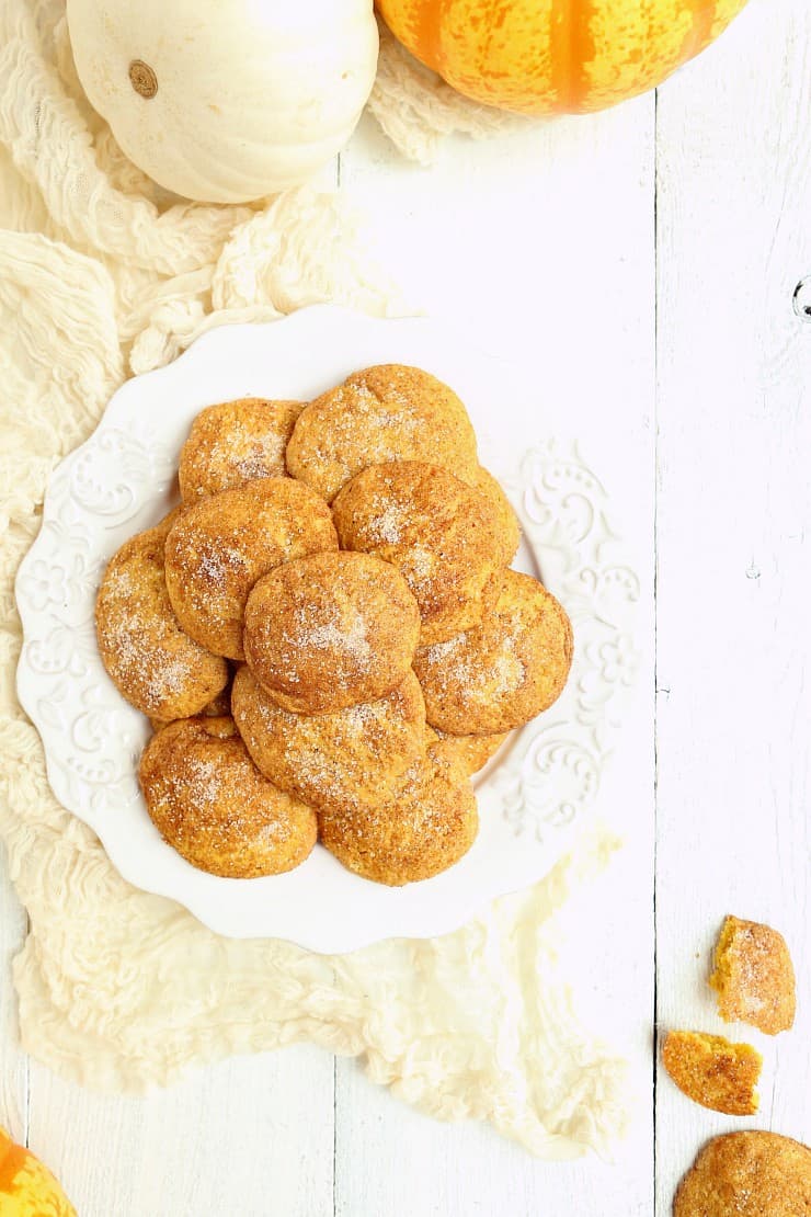 overhead shot of a pile of pumpkin snickerdoodles on plate with white wood background and pumpkins to decorate