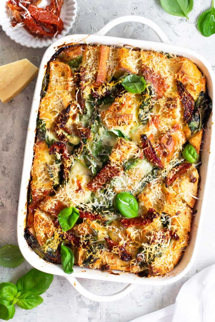 An overhead shot of a breakfast strata in a white dish topped with sun dried tomatoes and spinach