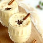 Two glasses of eggnog topped with cinnamon sticks and spices