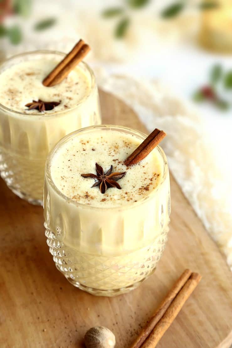 Two glasses of eggnog topped with cinnamon sticks and spices