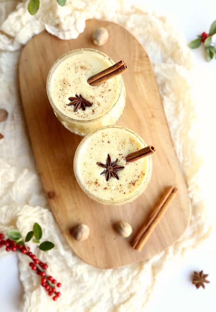 overhead shot of two glasses eggnog on wood tray with cinnamon sticks and spices 