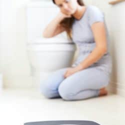 Sad young woman sitting on bathroom floor near scale