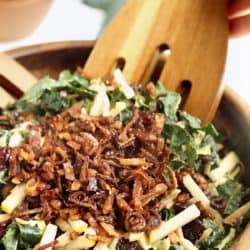 Close up image of Kale and Brusssels Sprouts Super Salad being tossed with wooden tongs in wooden salad bowl