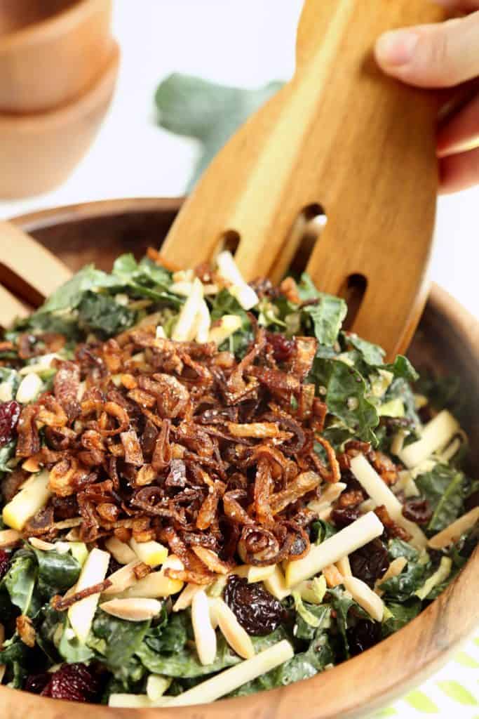 Close up image of Kale and Brusssels Sprouts Super Salad being tossed with wooden tongs in wooden salad bowl