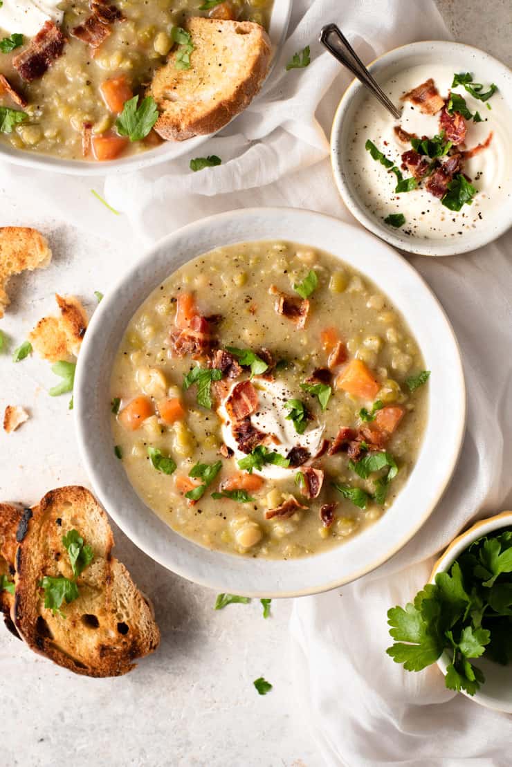 An overhead shot of split pea soup in two bowls topped with sour cream and bacon