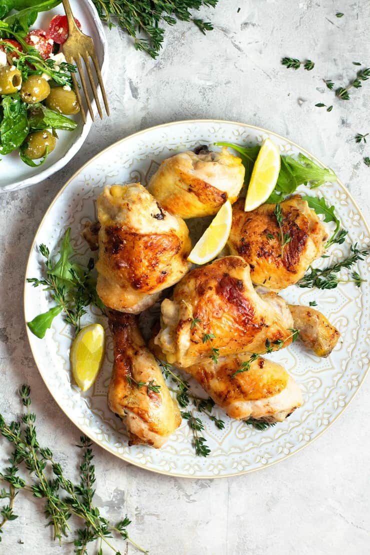 overhead shot of Greek Chicken on white plate with lemon wedges and fresh herb garnish