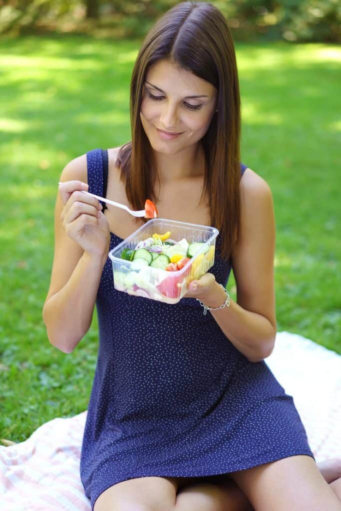 woman eating salad on picnic blanket
