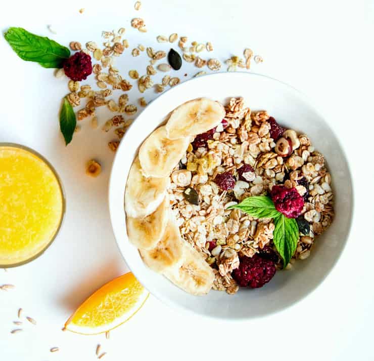 overheat shot of muesli and berries in white bowl with orange juice on the side